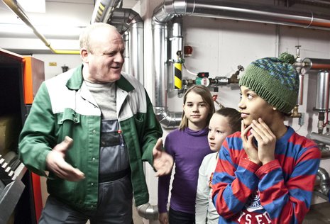 In der Grundschule am Kollwitzplatz zeigt ein Hausmeister Schulkindern die Heizungsanlage.